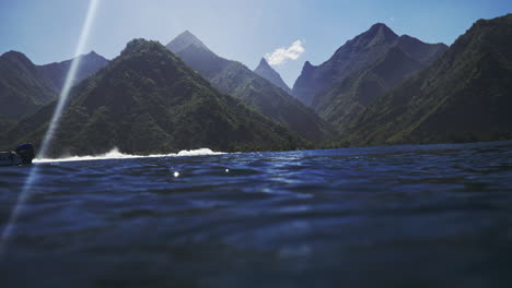Sunlight-shines-on-ocean-water-surface-as-waves-break-looking-into-tropical-green-mountain-valleys