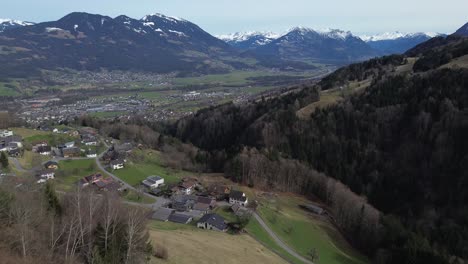 Drone-rise-up-and-reveals-amazing-view-over-Cityscape-surrounded-by-snow-covered-summits-in-Amerluegen,-Vorarlberg,-Austria