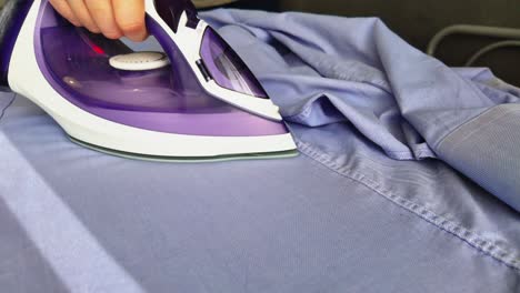 Hand-Holding-Electric-Iron-Ironing-Clothes-On-an-Ironing-Board