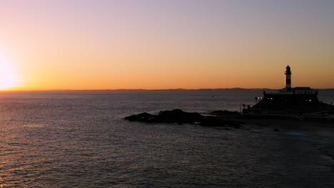 Aerial-view-of-Farol-da-Barra-illuminated-by-the-sun,-the-neighborhood-around-and-the-sea,-at-sunset,-Salvador,-Bahia,-Brazil