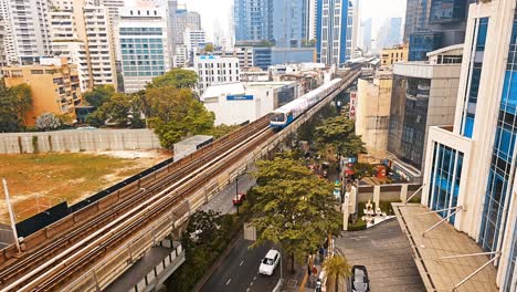 Skytrain-moving-from-the-upper-right-side-to-the-lower-left-side-of-the-frame,-passing-through-the-main-thoroughfare-of-Sukhumvit-street,-in-Bangkok,-Thailand