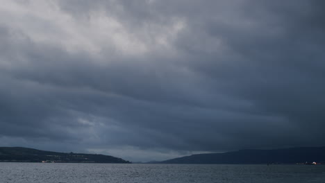 Heavy-dark-clouds-over-seaside-town-and-water,-dark-evening-light