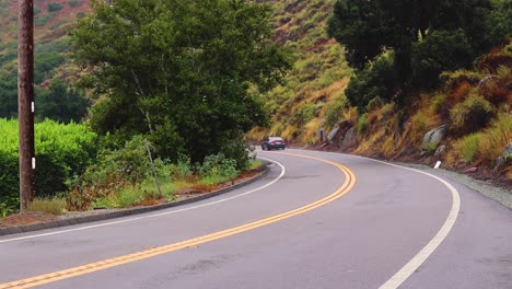 Two-cars-speed-along-mountain-roads,-trailing-a-continuous-line-through-scenic-landscapes