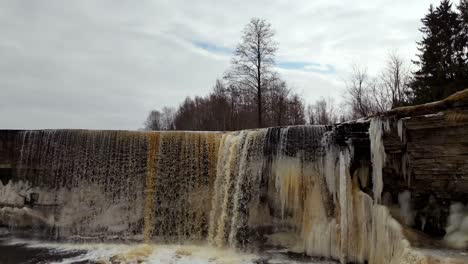Partly-frozen-Jegala-Waterfall-on-cloudy-winter-day,-aerial-dolly-out