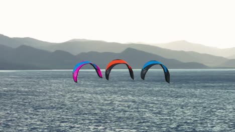 Three-Kiteboarding-Kites-Flying-Through-The-Air,-Vast-Open-Tropical-Ocean,-Tropical-Vacation,-No-People,-Mountains-In-Background,-Slow-Motion,-Afternoon-Soft-Light