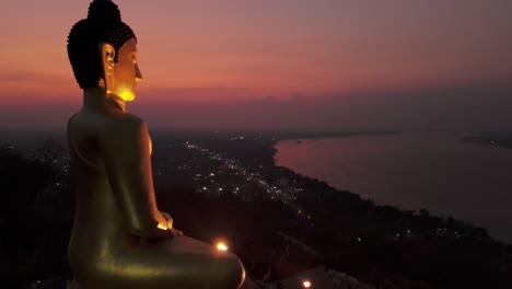 Golden-Buddha-overlooking-Mekong-river-vibrant-sunset,-Pakse,-Laos