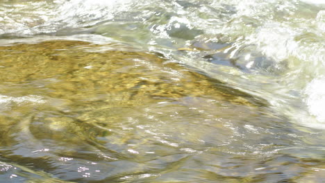 Crystal-clear-drinking-water-flows-between-stones-of-a-river-in-sunlight