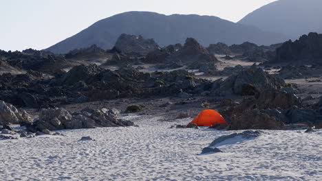 Orange-tent-alone-on-rugged-rocky-sand-beach-in-remote-coast-of-Chile