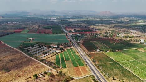 Bird's-eye-view-captures-the-rural-landscape-of-Sangklaburi-in-Thailand,-with-a-road-dividing-farms-and-plantations
