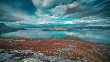 Stormy-clouds-whirl-above-the-calm-mirrorlike-fjord-and-autumn-tundra-in-the-timelapse-video