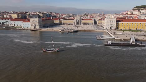 Aerial-pullback-as-Tagus-river-water-flows-and-sailboat-drives-up-in-front-of-square-in-Lisbon-Portugal