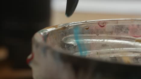 Wiping-paintbrush-on-the-edge-of-glass-jar-from-excess-water-in-artistic-process,-closeup