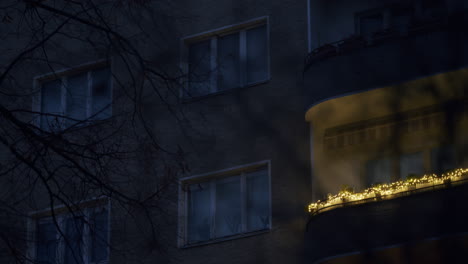 Christmas-lights-on-balcony-of-residential-building-in-low-light,-with-leafless-tree-in-front