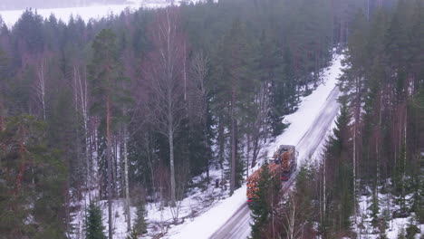 Truck-transports-harvested-timber-logs-on-snowy-forest-road,-telephoto-aerial