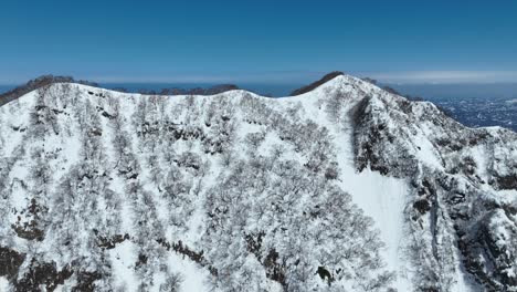 Aerial-fly-over-shot-of-top-of-Myoko-Mountain-Summit,-Japans-coast-line-and-ocean-sea-visible-in-background