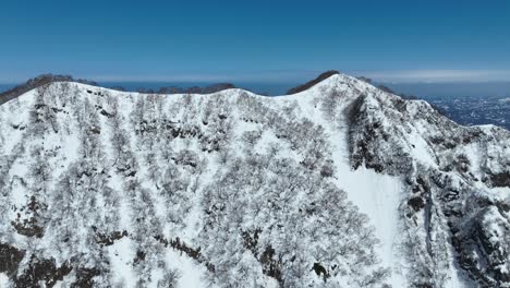 Vuelo-Aéreo-Sobre-La-Cima-De-La-Cumbre-De-La-Montaña-Myoko,-La-Línea-Costera-De-Japón-Y-El-Mar-Del-Océano-Visible-En-El-Fondo