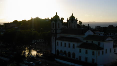 Vista-Aérea-De-La-Parte-Trasera-De-La-Iglesia-Nosso-Senhor-Do-Bonfim,-El-Vecindario-Y-El-Océano-Al-Fondo,-Al-Atardecer,-Salvador,-Bahía,-Brasil