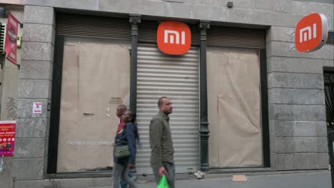 Pedestrians-walk-past-a-closed-Chinese-multinational-technology-and-electronics-brand-Xiaomi-flagship-store-in-Madrid,-Spain