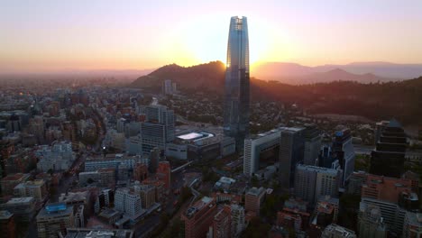 Aerial-view-circling-the-Gran-Torre-Santiago-tower,-dramatic-sunset-in-Chile