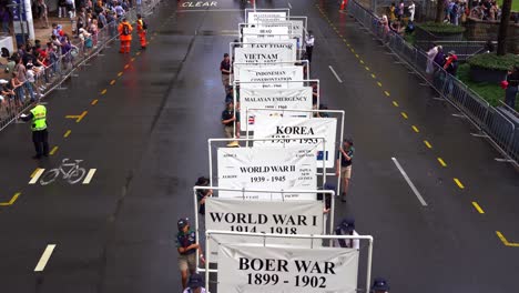 Freiwillige-Halten-Das-Banner,-Das-Die-Historischen-Ereignisse-Des-Krieges-Darstellt,-Während-Sie-Während-Der-Traditionellen-Anzac-Day-Parade-Durch-Die-Straßen-Der-Stadt-Brisbane-Marschieren