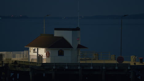 Pier-and-cabin-in-evening-light,-with-water-and-distant-flashing-lights-behind,-static