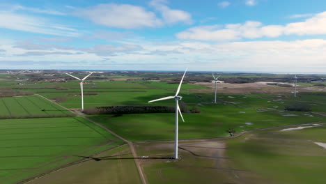 Aerial-drone-shot-of-wind-turbines-amidst-wet,-green-fields-during-early-springtime