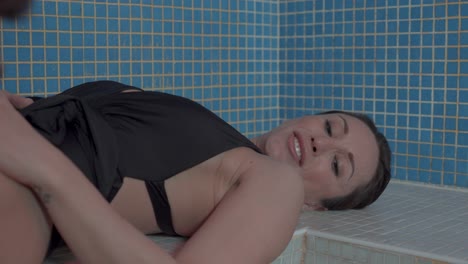 A-woman-in-a-hammam-with-a-black-one-piece-swimsuit,-is-lying-on-the-blue-mosaic-tiled-bench