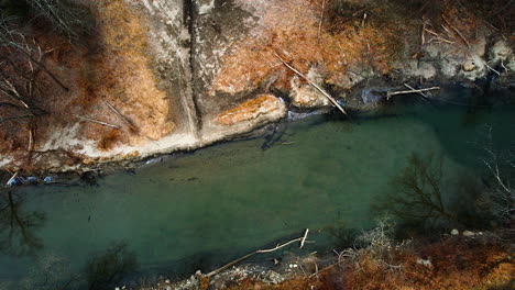 Green-sediment-in-water-of-shallow-river-stream-with-sloped-silty-sandy-banks,-drone-top-down
