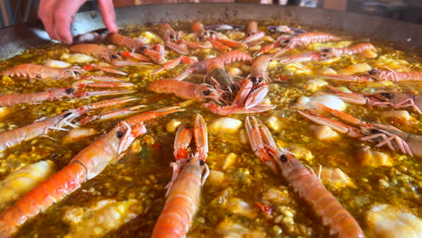 Cooking-a-huge-traditional-Spanish-seafood-Paella-dish-with-shrimps,-St-Jacques-scallops-and-Cigala-Norway-lobsters-Nephrops-norvegicus,-cooked-rice-with-seafood,-Marbella-Spain,-4K-shot