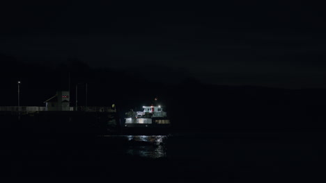 Ferry-boat-driving-away-from-pier-at-night,-distant-static-shot