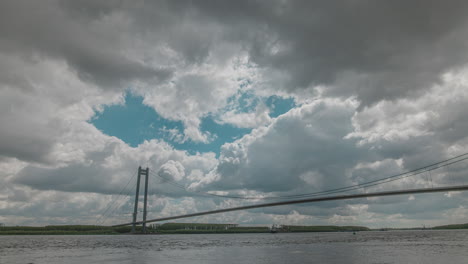 Timelapse-with-cloudy-skies-atop-a-tall-suspended-bridge-over-a-big-river,-HDR