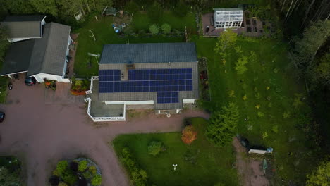 High-angle-drone-shot-of-sunlit-solar-cells-on-a-modern-family,-fall-evening