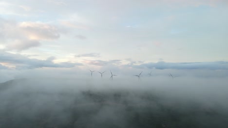 Wind-turbines-on-mountains,-generate-green-energy,-surrounded-by-clouds-in-the-sky