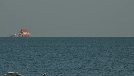 Seen-from-afar-a-Buddhist-temple-in-the-middle-of-the-sea-as-seabirds-fly-around,-Thailand