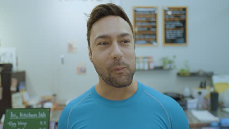 Cheerful-Man-in-30s-Eating-Fresh-Salad-Smiling-Looking-at-Camera-Inside-Small-Cafe