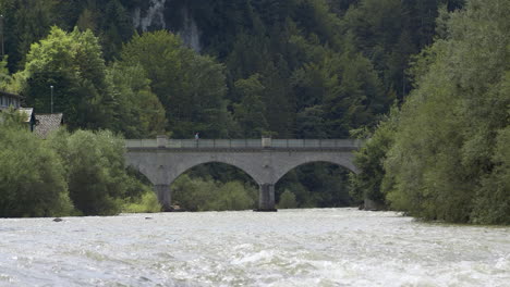 Man-walks-over-a-bridge,-historic-stone-bridge-over-a-picturesque-river