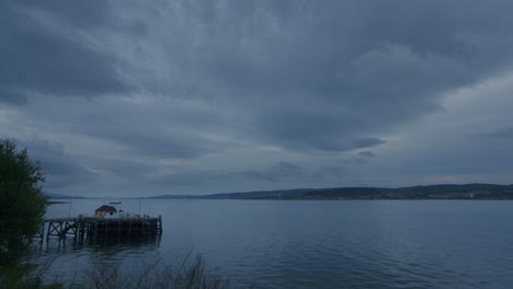 Timelapse-of-pier-and-sea-and-sky-and-distant-town,-the-clouds-come-rushing-in