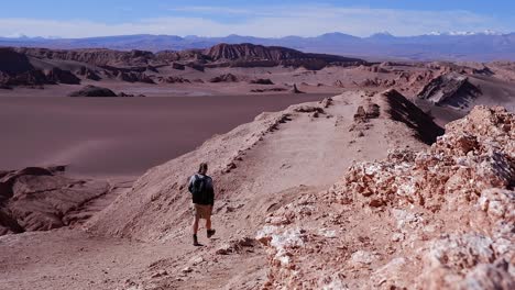 Stunning-natural-desert-viewpoint,-male-hiker-walks-on-gravel-ridge