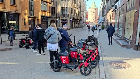 Un-Grupo-De-Scooters-Rojos-Están-Estacionados-En-Una-Acera-Frente-A-Un-Edificio