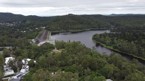 Drone-flying-towards-a-water-reservoir-in-Australia-showing-a-dam-wall-and-the-green-bushland-around-the-lake