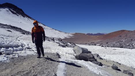 Man-hikes-on-cool,-crisp-day-in-snowy-gravel-mountain-plateau-in-Chile