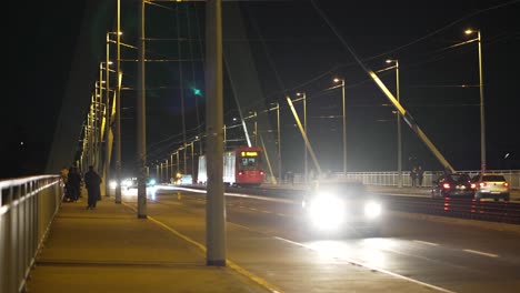 A-local-train,-cars-and-people-passing-by-the-Severinsbrücke-in-Cologne,-Germany-by-night