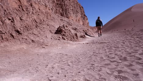 Lone-man-hikes-along-red-sand-desert-rock-cliff,-Atacama-region,-Chile