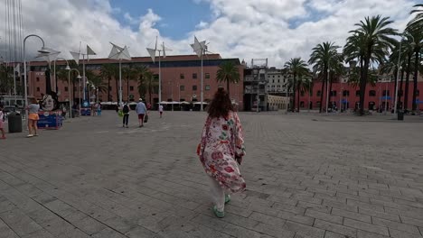 Following-shot-showing-lady-walking-through-paved-town-square-in-Italy,-wearing-patterned-clothing