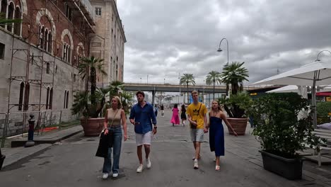 Handheld-clip-walking-through-town-square,-with-multiple-passersby-walking-closely,-past-market-stalls-and-traditional-buildings