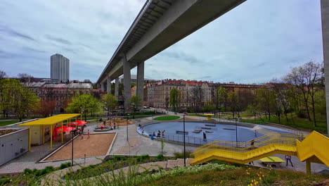 Bridge-road-Crosses-above-Czech-Republic-Prague-City-urban-park-infrastructure-with-people-relaxing-and-hanging-out-in-urban-area,-cloudy-skyline