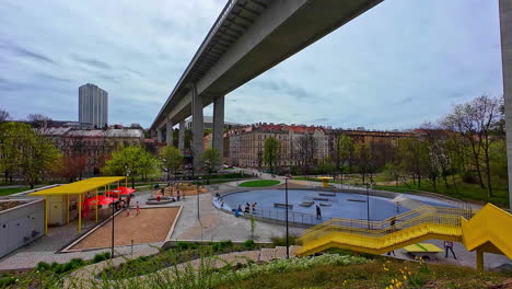 Die-Brückenstraße-Führt-über-Die-Städtische-Parkinfrastruktur-Der-Tschechischen-Stadt-Prag,-In-Der-Sich-Menschen-Entspannen-Und-Im-Stadtgebiet-Herumhängen,-Wolkige-Skyline