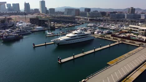 Aerial-drone-shot-of-a-megayacht-parked-in-the-port-of-Barcelona-with-views-of-the-city-in-the-background-on-a-sunny-day