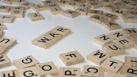 Right-hand-places-three-Scrabble-tiles-onto-table-forming-word-WAR