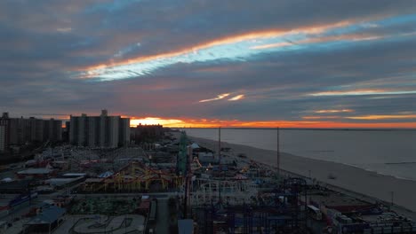 An-aerial-view-of-Coney-Island-amusement-park-in-Brooklyn,-NY-during-a-cloudy-but-colorful-sunrise